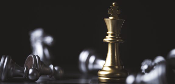 Bronze chess piece with fallen silver pieces around it.